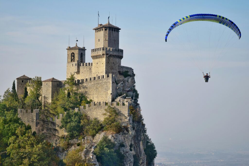 Guaita Tower in San Marino with a paraglider soaring nearby, showcasing a blend of adventure and history.